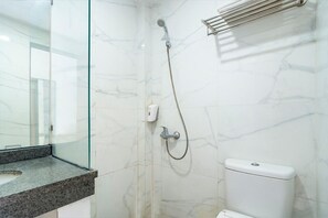 A bathroom with a glass shower enclosure, a marble wall, and a white toilet. - Life Hotel Sidoarjo (Sidoarjo)