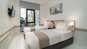 A hotel room with two beds, a television, a painting, and a window with a view of the street. - Life Hotel Sidoarjo (Sidoarjo)