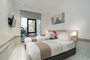 A hotel room with two beds, a television, a painting, and a window with a view of the street. - Life Hotel Sidoarjo (Sidoarjo)