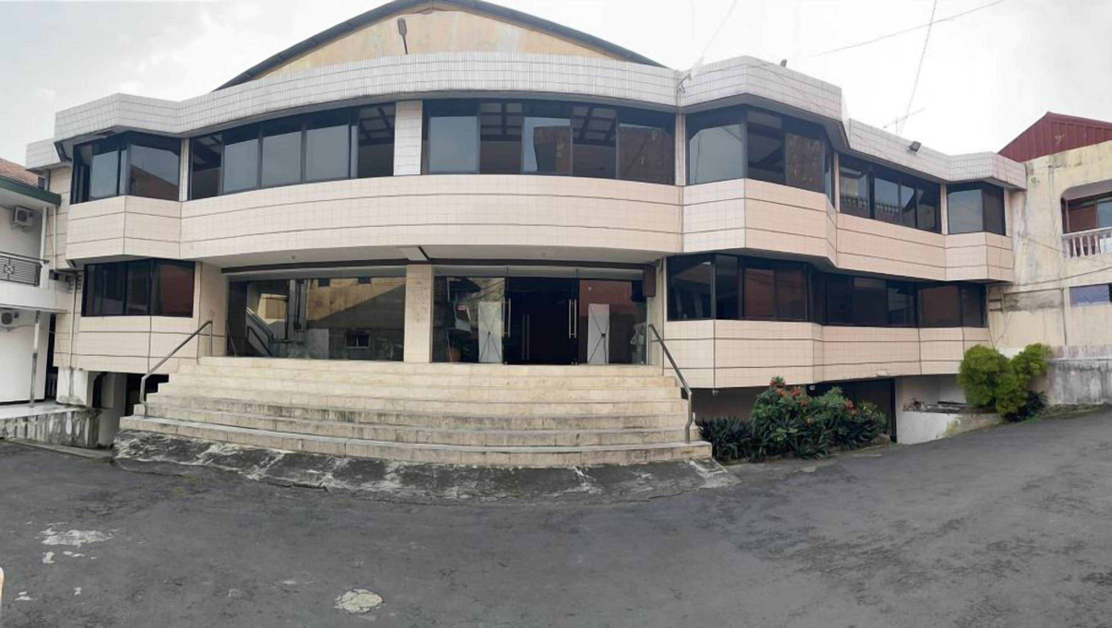 Un edificio a più piani con tetto piatto, ampie finestre e un ingresso centrale con gradini.