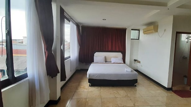 Ein Hotelzimmer mit einem Bett, einem Fenster mit Vorhängen, einer Tür und einem kleinen Tisch.
