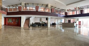 Un vestíbulo amplio con techo alto, una escalera y una recepción.