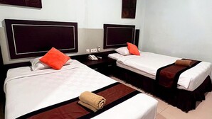 Quarto de hotel com duas camas, cada uma com travesseiro e cobertor, mesa de cabeceira e ar condicionado fixado na parede.