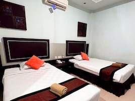 Habitación de hotel con dos camas, cada una con una almohada y una manta, una mesita de noche y un equipo de aire acondicionado en la pared.