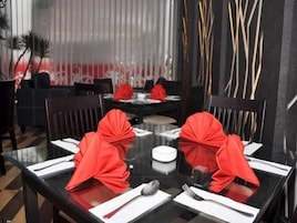 Comedor con una mesa para cuatro, con cubierta de vidrio y adornos de servilletas rojas.