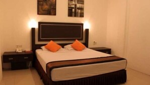 Uma cama bem arrumada com cabeceira de madeira, duas mesas de cabeceira com abajures e uma obra de arte na parede.