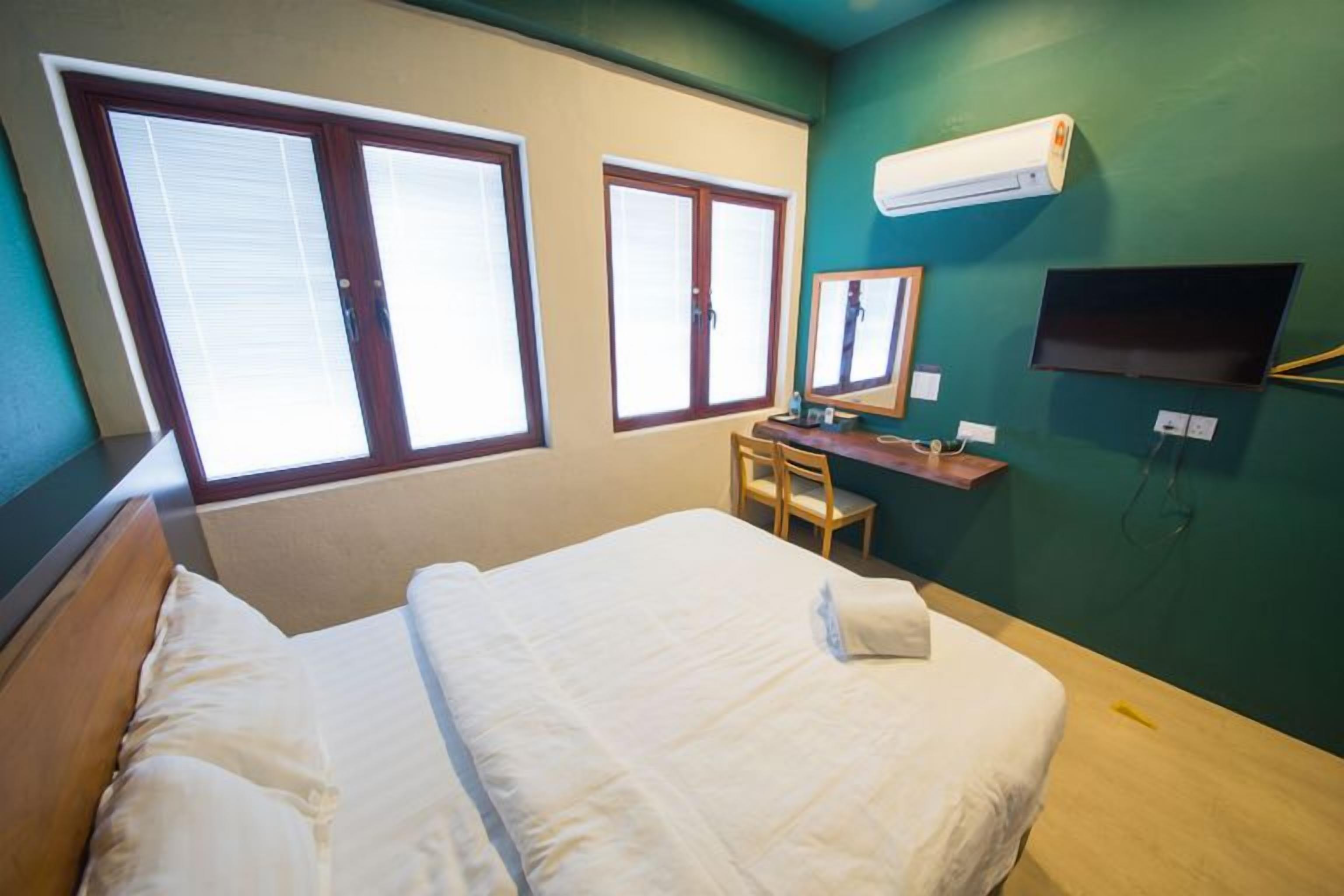 A hotel room with a bed, a desk, a chair, a television, and two windows.