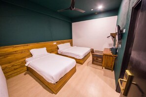 Ein Hotelzimmer mit zwei Holzbetten, einem Schreibtisch mit Stuhl, einem Deckenventilator und einem an der Wand befestigten Fernseher.