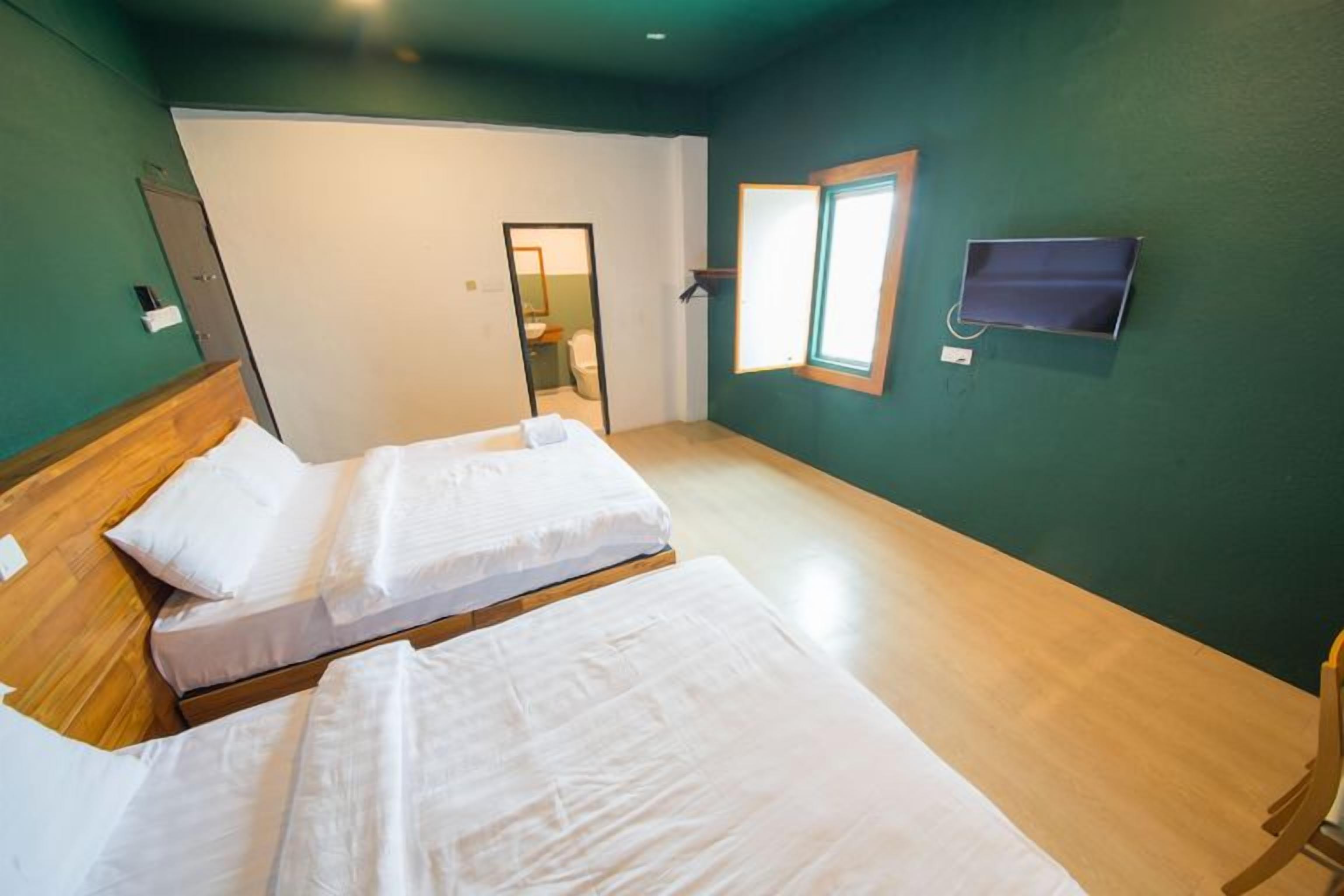 A room with two beds, a wooden headboard, a window, and a mirror on the wall.