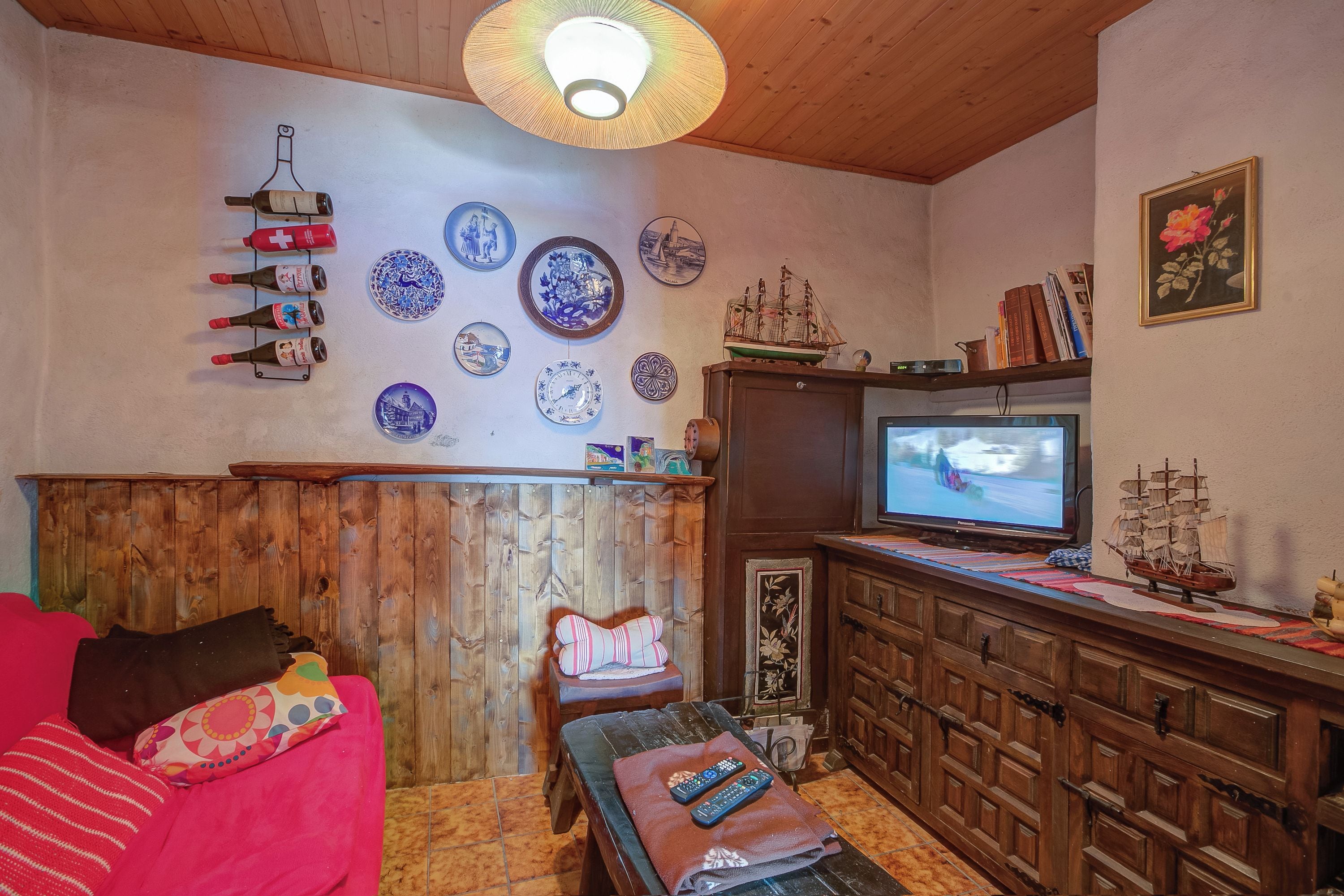 Un salon chaleureux avec un plafond en bois, un téléviseur et diverses assiettes décoratives accrochées au mur.