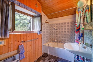 Un baño con paredes de madera, una bañera, un lavabo y una ventana con vista a árboles.