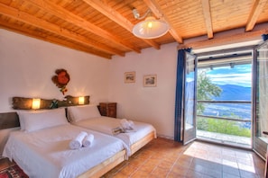 Un dormitorio con dos camas, techo de madera, un ventanal con vistas y una lámpara fijada a la pared.