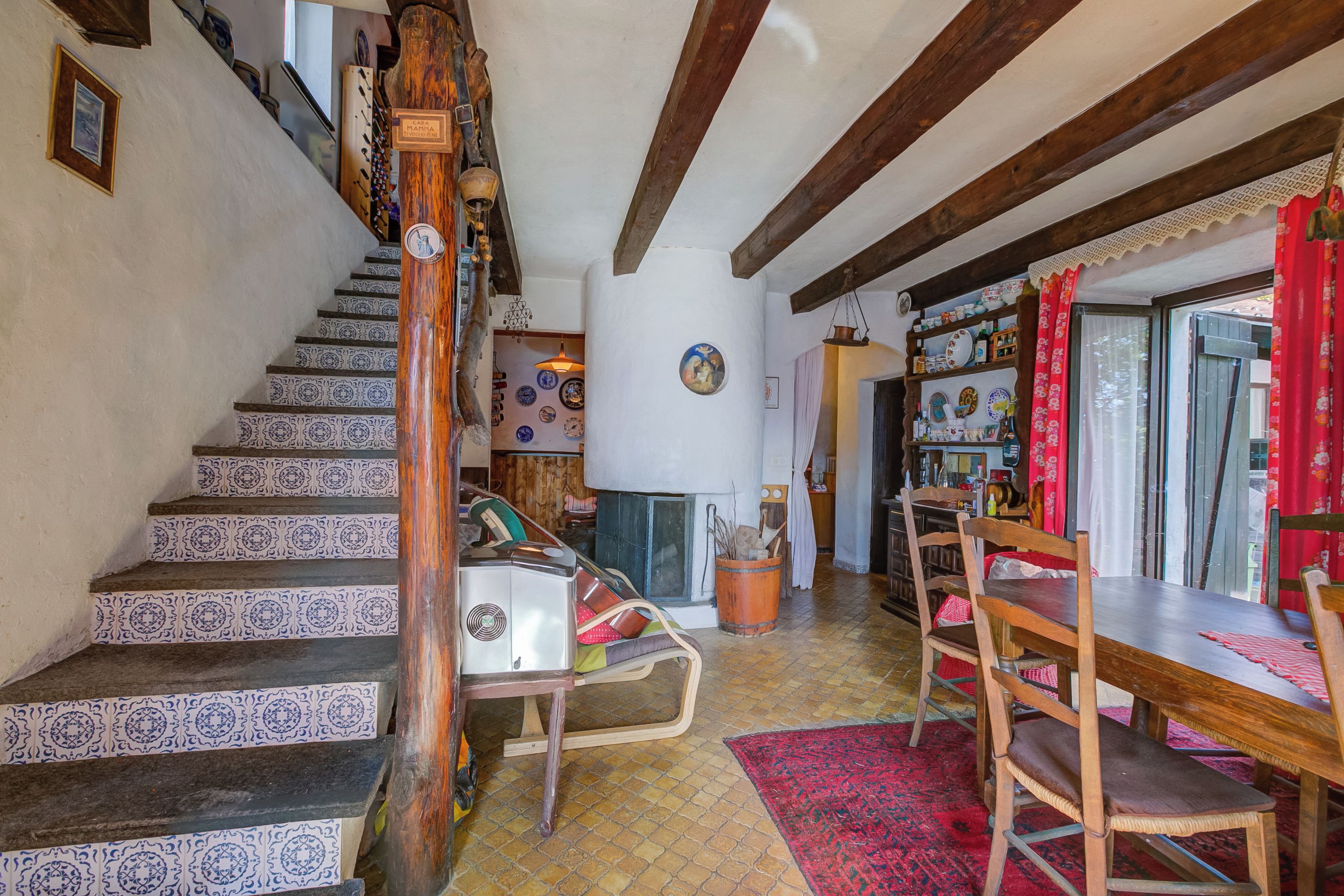 A staircase with patterned tiles, a wooden chair, a dining table with chairs, and a red rug.