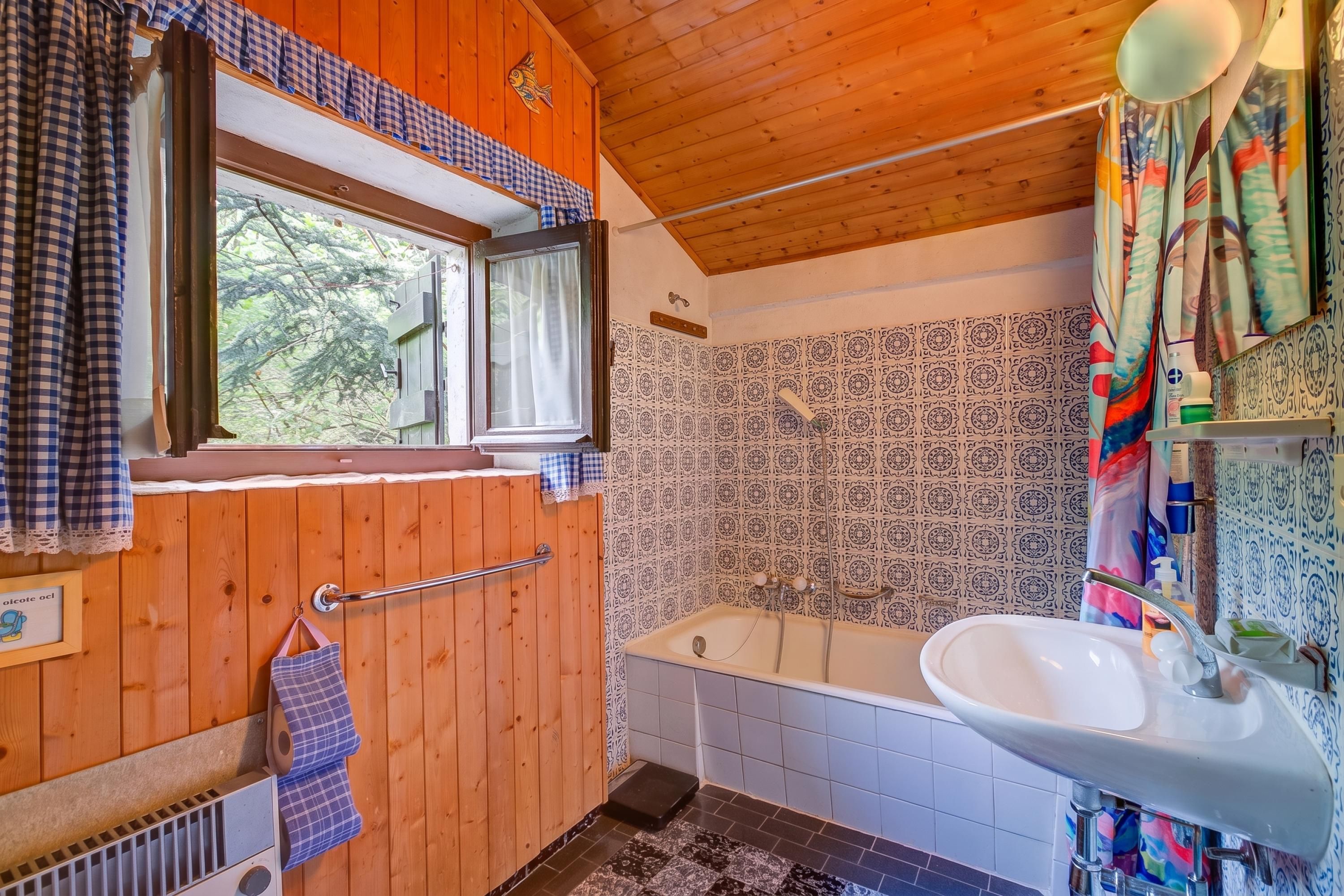Ein Badezimmer mit Holzvertäfelung, einer Badewanne, einem Waschbecken und einem Fenster mit Blick auf Bäume.