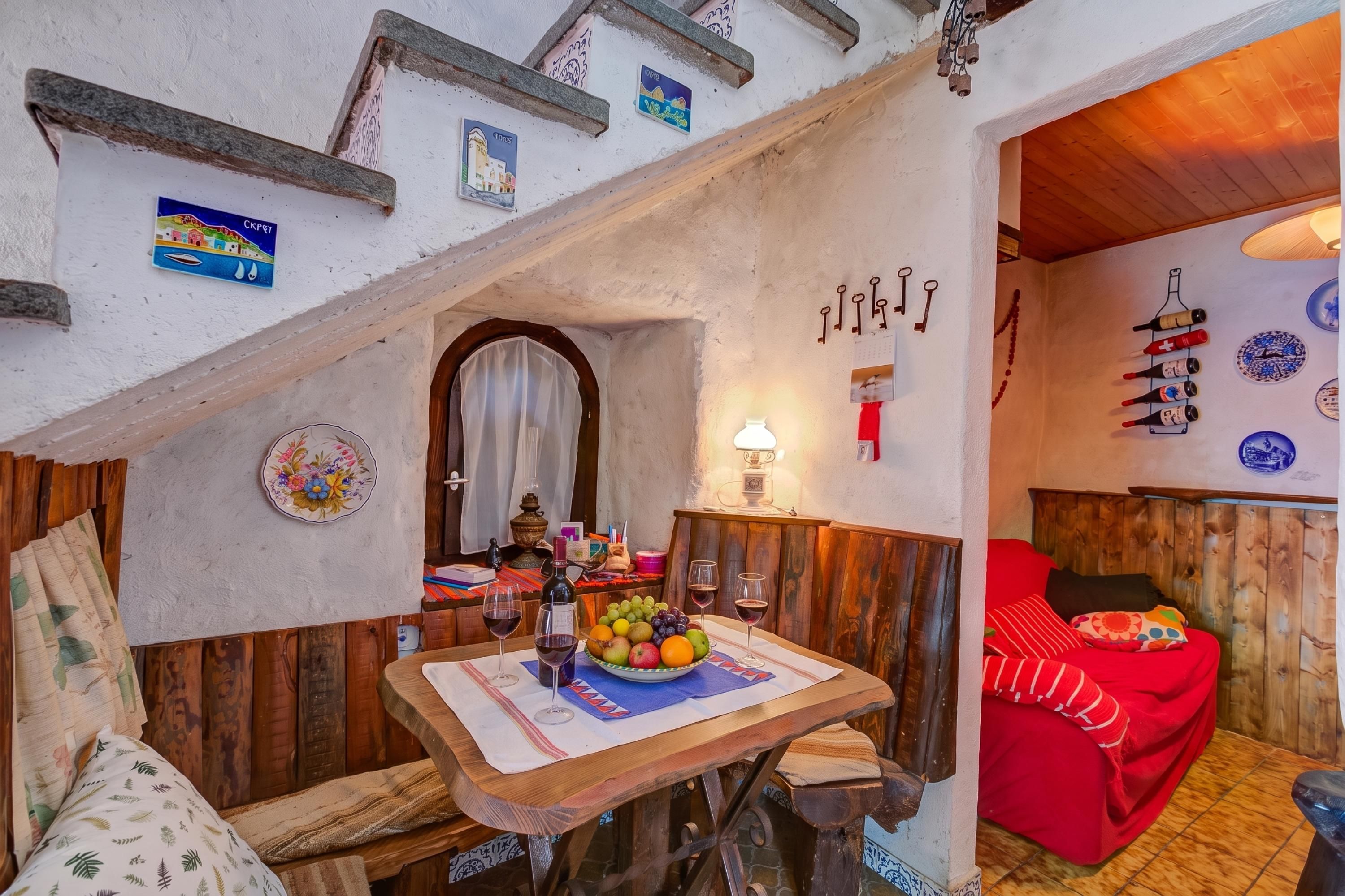A rustic interior with a wooden table set for dining, a red sofa, and a staircase leading to an upper level.