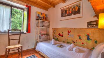 A bedroom with a wooden ceiling, a bed with white bedding, a chair, a window with a view of trees, and a shelf with items.