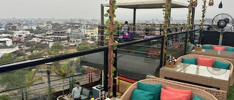 A rooftop bar with wicker furniture, a glass table, and a view of the cityscape.
