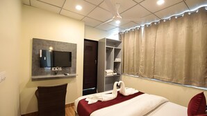 Een hotelkamer met een bed, een aan de muur bevestigde televisie, een kledingkast en een raam met gordijnen.