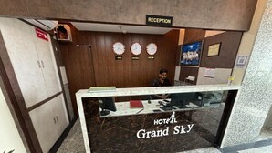 Een hotel receptiebalie met een marmeren aanrecht, klokken die verschillende tijdzones aangeven, en een receptieteken erboven.