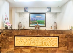 A reception desk with a framed painting of a mountain landscape, a statue, and decorative vases. - Hotel Lumba-lumba inn Waru (Surabaya)