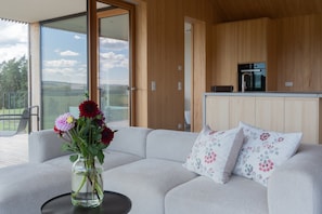Ett modernt vardagsrum med en soffa, en vas med blommor och utsikt över naturen.