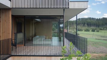 Un edifici modern amb un balcó, grans finestres i vista a un bosc.