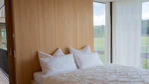 A bedroom with a wooden headboard, a large bed with white bedding, and a view of a green landscape through a window. - Apartment 'Ruhige Dachgeschoss-Wohnung' with Panoramic Green View, Balcony and Parking (Bad Dürrheim)