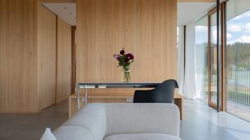 Habitación moderna con pared de madera, una mesa de vidrio con un jarrón de flores, una silla negra y un ventanal grande.