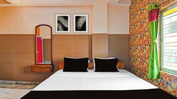 Une chambre d’hôtel avec un lit, deux oreillers, une table de chevet, un miroir et deux tableaux encadrés accrochés au mur.