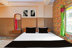 Una habitación de hotel con una cama, dos almohadas, una mesita de noche, un espejo y dos cuadros en la pared.