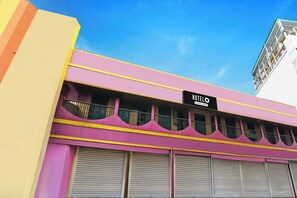 A hotel with a sign indicating it is company-serviced, featuring a pink facade with yellow trim and multiple balconies.
