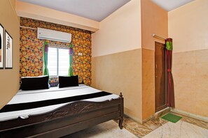 A bedroom with a bed, a window with curtains, an air conditioning unit, and a door.