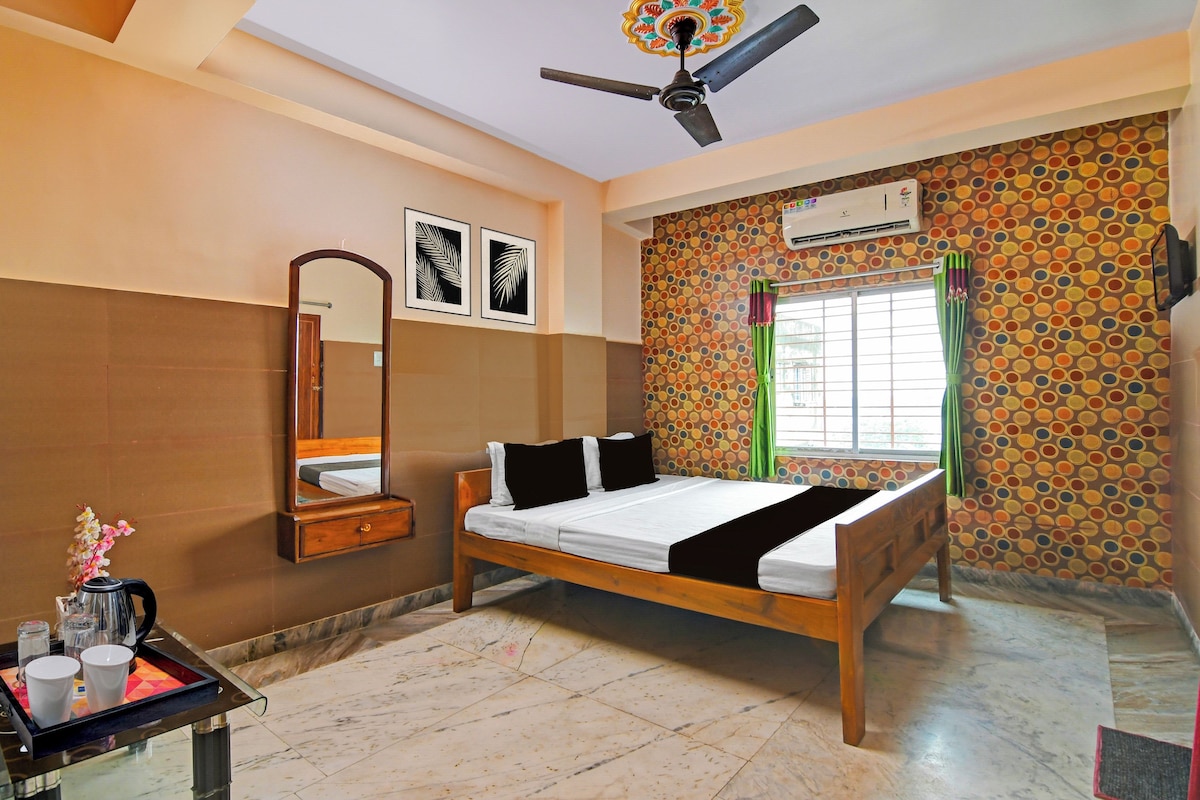 A hotel room with a bed, a mirror, a ceiling fan, a window with curtains, and a wall with a circular pattern.