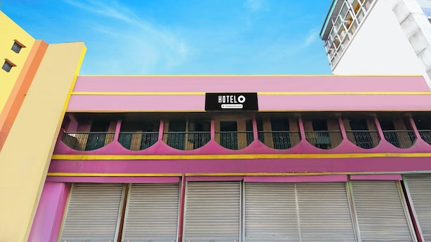 Ein Hotel mit einer rosa und gelben Fassade, einem Schild mit dem Hotelnamen und heruntergelassenen Fensterläden.