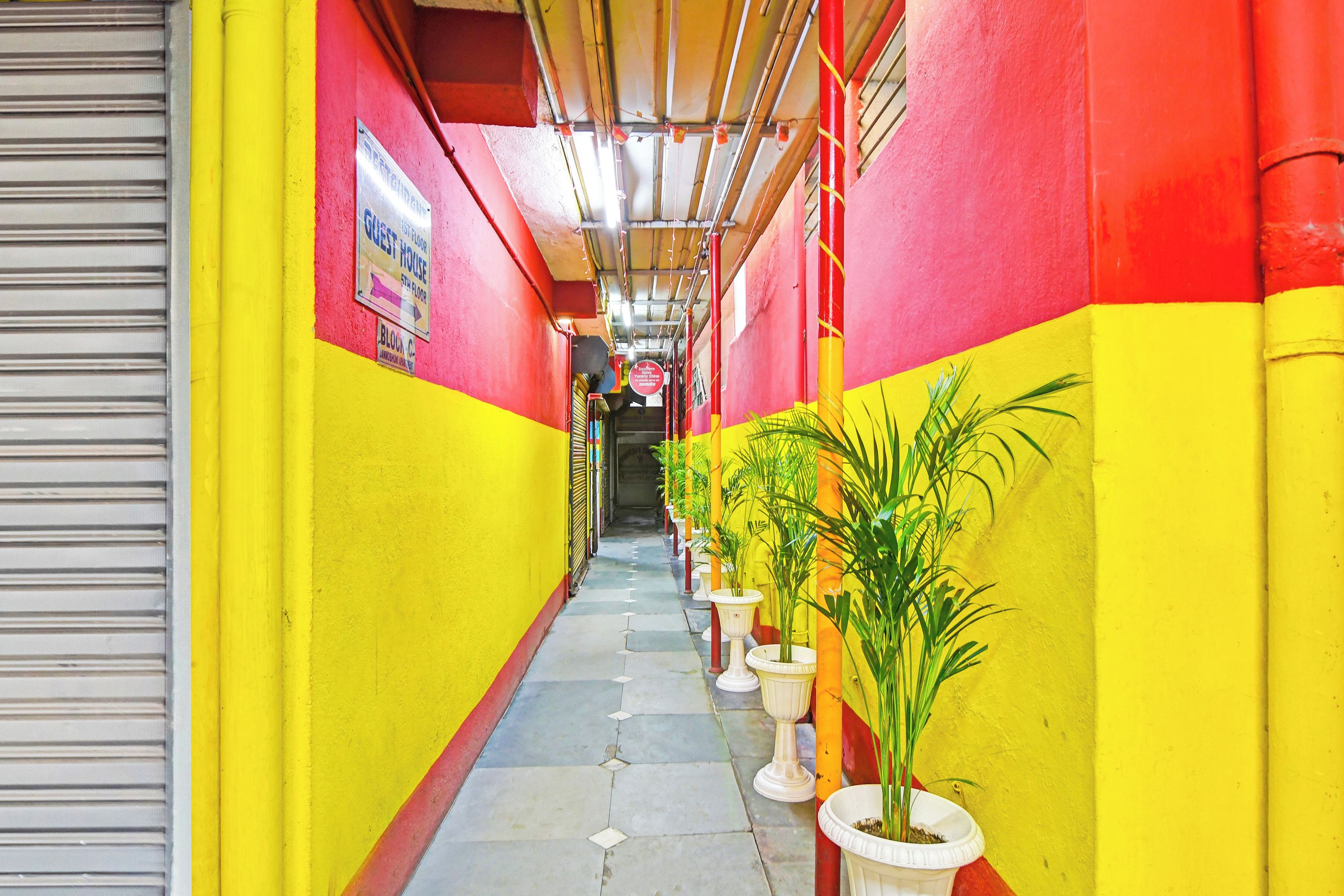 A corridor with a yellow and red color scheme, potted plants, and a sign indicating a guest house on the 5th floor.