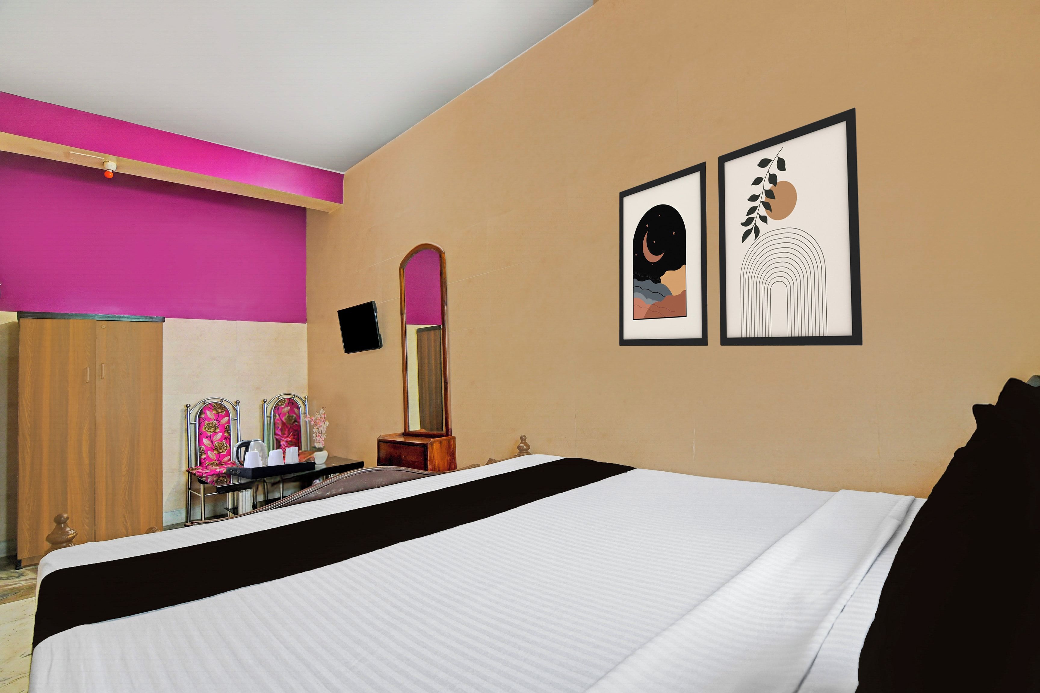 A hotel room with a bed, a vanity with a mirror, and two framed artworks on the wall.