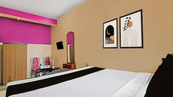 A hotel room with a bed, a vanity with a mirror, and two framed artworks on the wall.