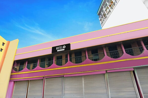A hotel with a pink facade, a sign indicating it is company-serviced, and multiple windows with metal railings.