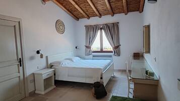 A bedroom with a bed, bedside tables, a small bench, a window with curtains, and a ceiling with wooden beams.