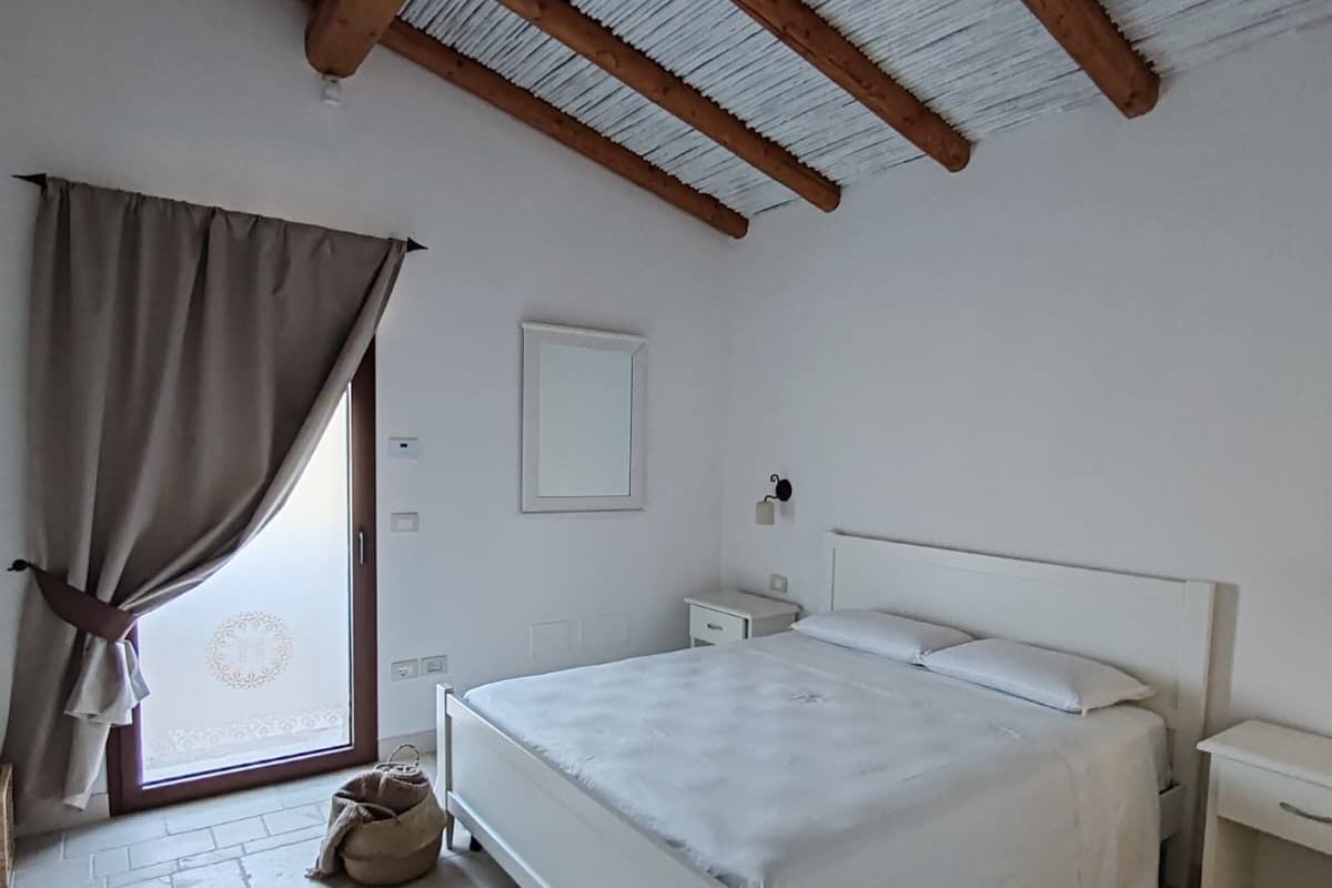 Ein Schlafzimmer mit einem Bett, Nachttischen, einem Fenster mit Vorhängen und einer Holzbalkendecke.