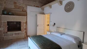 Un dormitorio con chimenea de piedra, una cama con ropa blanca y una puerta blanca que da a otra habitación.