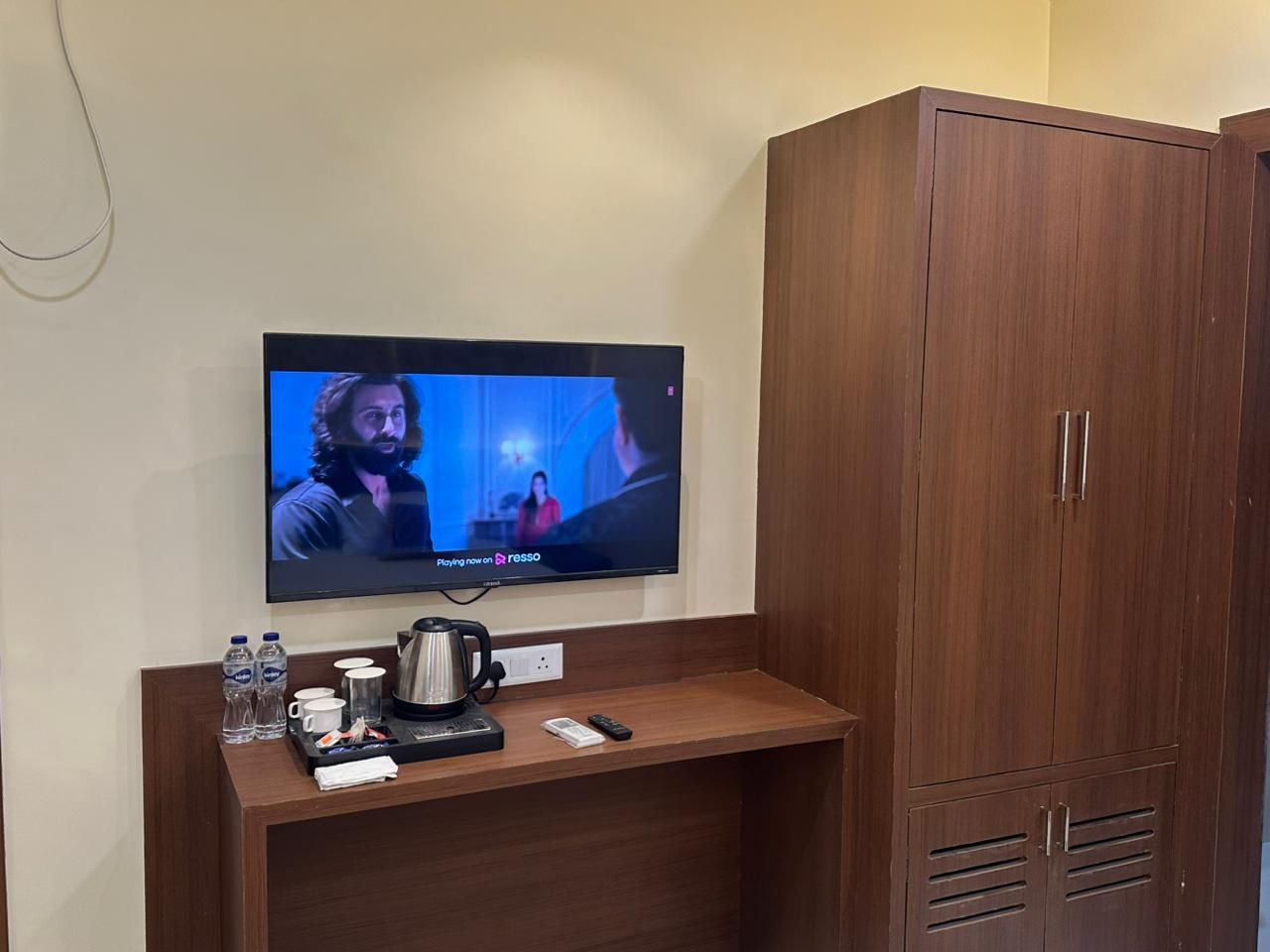A television mounted on a wall with a wooden cabinet beside it.