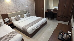 A hotel room with two beds, a desk, a wardrobe, and a coffee table with a kettle and remote control. -  Aristo Inn B&B (Varanasi)