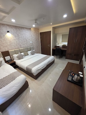 Habitación de hotel con dos camas, un escritorio, un armario y una mesa de centro con tetera y control remoto.