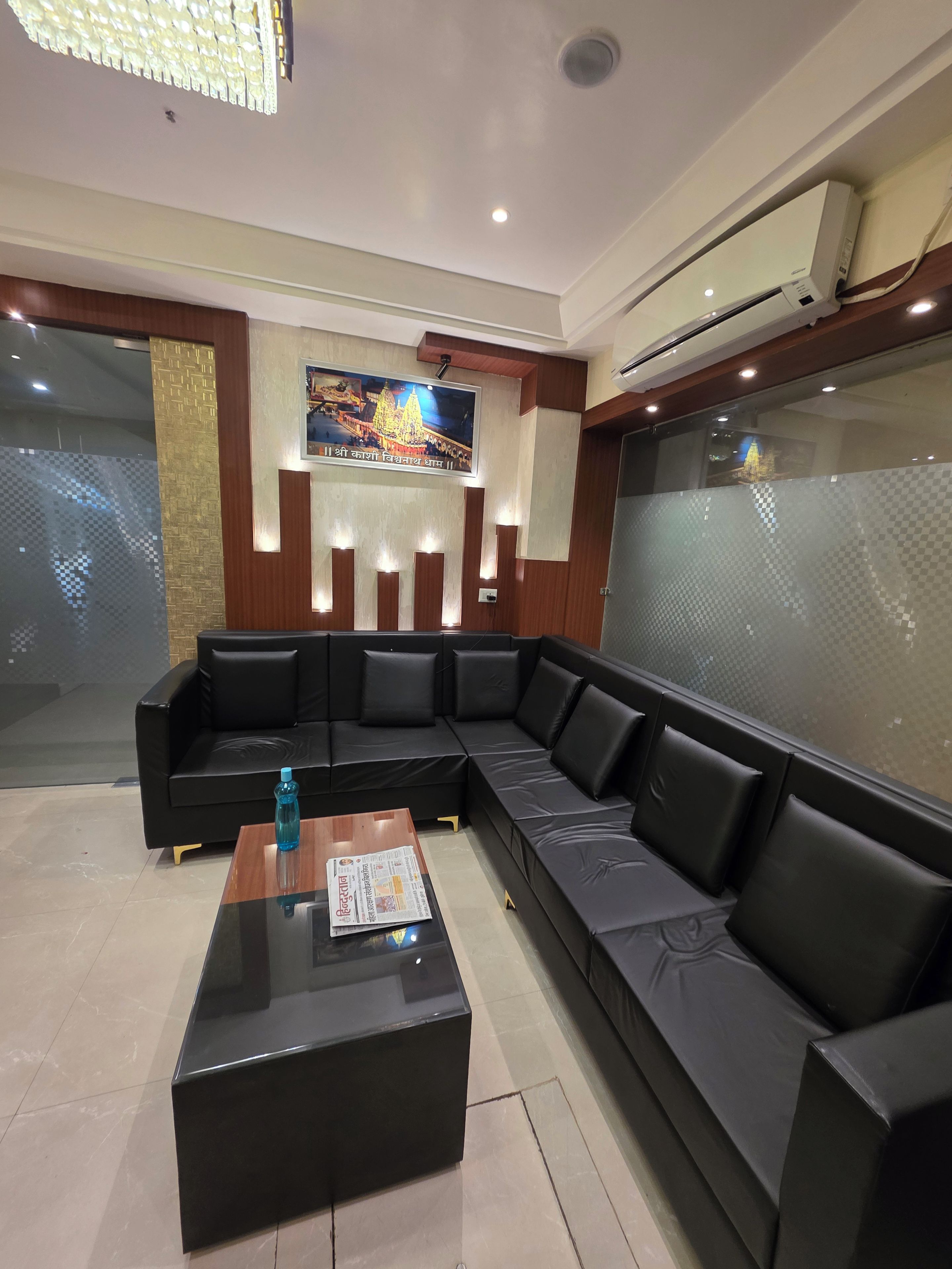 A modern hotel lobby with a black leather sofa, a glass coffee table, and a framed picture on the wall.