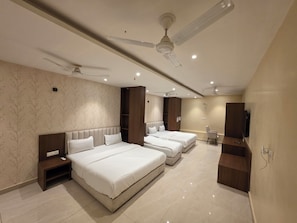 Habitación de hotel con dos camas, televisor, escritorio y ventilador de techo.