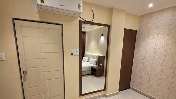 A hotel room with a bed, bedside table, and a large mirror. There is an air conditioning unit mounted on the wall. -  Aristo Inn B&B (Varanasi)