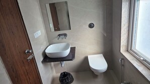 A bathroom with a wooden door, a white sink, a mirror, a toilet, and a shower area. -  Aristo Inn B&B (Varanasi)