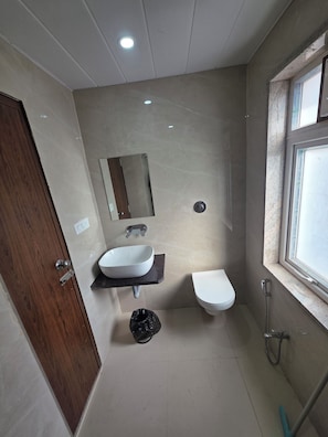 Un baño con puerta de madera, lavamanos blanco, espejo, inodoro y zona de ducha.