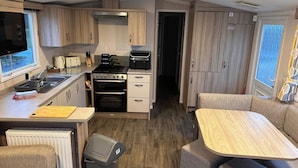 Una cocina compacta con estufa, horno y lavamanos, un comedor con mesa y sillas, y vistas a través de una puerta abierta.